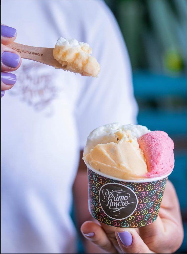 Mão segurando copo Primo Amore com gelato de creme e morango
