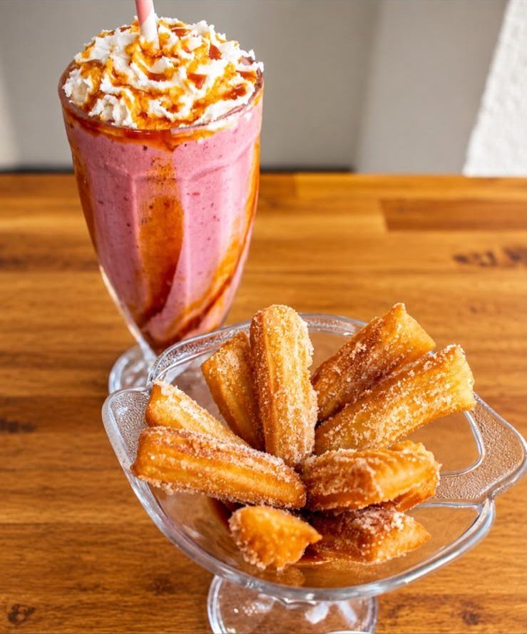 Milkshake com chantilly e calda ao lado de churros
